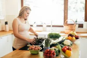 pregnant woman cutting fresh produce in kitchen